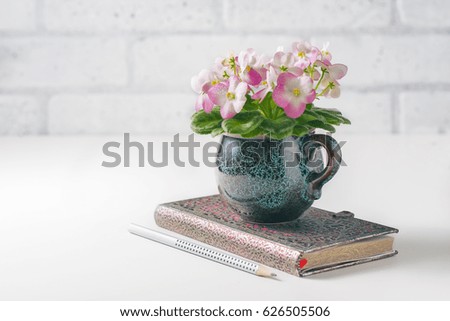Clean notebook, eyeglasses, Pink and White African Violet on white table from above. Female working desk.