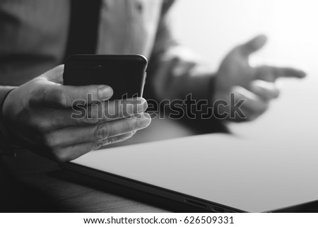 close up of businessman working with mobile phone and laptop computer on wooden desk in modern office with virtual reality icon diagram,black and white     