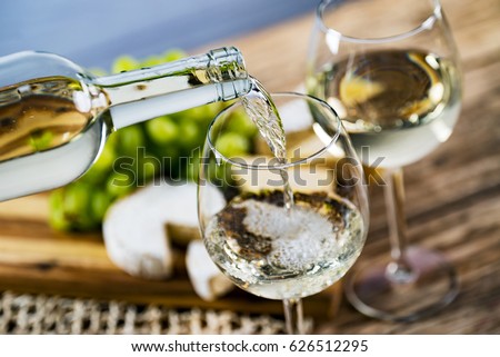 Pouring white wine into the glass against wooden table Royalty-Free Stock Photo #626512295