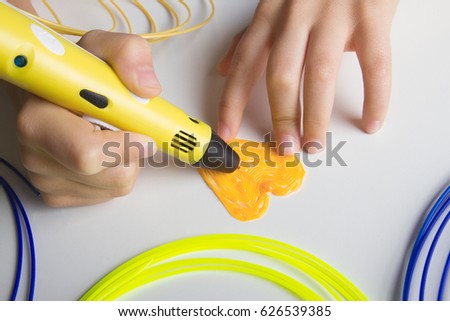 Kid hand holding yellow 3D printing pen and making heart. Top view.
