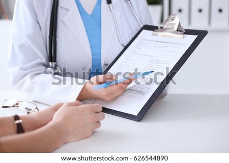 Close up of a doctor and  patient hands while physician pointing into medical history form at clipboard. Medicine and health care concept