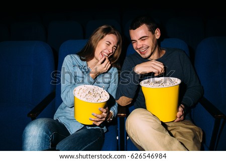 Cinema day. Happy young couple watching comedy movie in cinema, smiling.