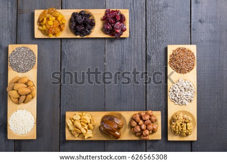 sun dried berry fruits, nuts and seeds on bamboo serving trays, frame composition, black wood table background