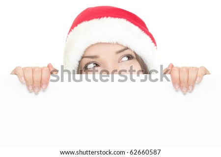 Girl in Santa peeking over paper sign board looking up. Cute funny photo closeup of christmas woman with copyspace. Isolated on white background.