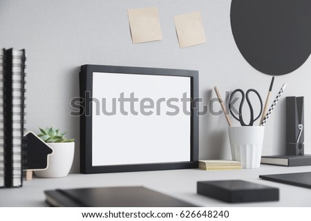 Creative desk with blank picture frame or poster, desk objects, office supplies, books and plant on a gray background. Creative desk.