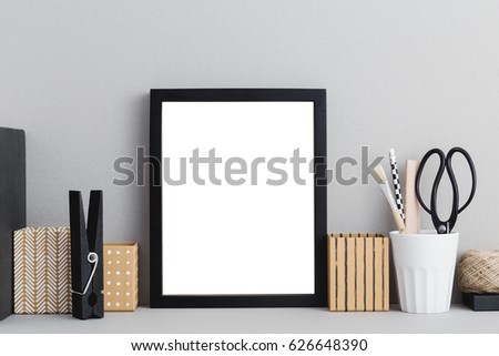 Black empty poster frame and office supplies on gray background,