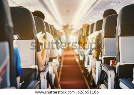 passenger seat, Interior of airplane with passengers sitting on seats and stewardess walking the aisle in background. Travel concept,vintage color,selective focus Royalty-Free Stock Photo #626651186