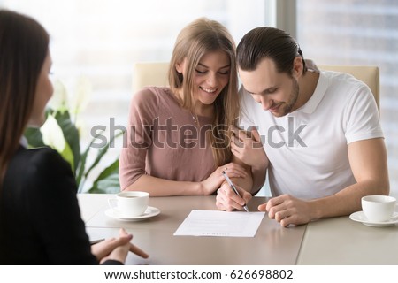 Smiling couple agreed to sign prenuptial contract, handsome man putting signature on document while sitting together with his wife, taking bank loan, health insurance, signing financial papers 