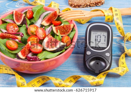 Fruit and vegetable salad, glucose meter with result of measurement sugar level and tape measure, concept of diabetes, diet, slimming, healthy lifestyles and nutrition Royalty-Free Stock Photo #626715917