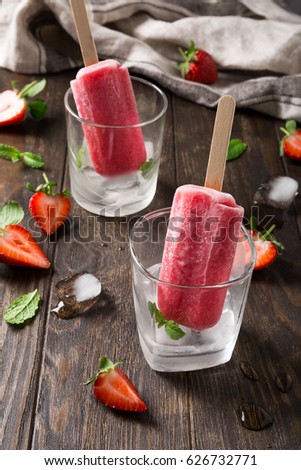 Glass with strawberry popsicles, strawberries and mint on old wooden background. Summer food concept