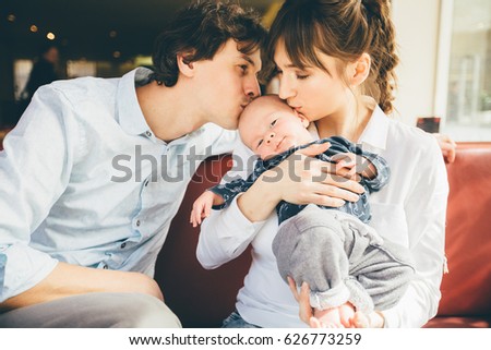 Happy parenthood: young parents kissing their sweet baby boy in cozy cafe interior.