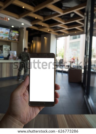 Man hand holding touch screen smart phone with white blank empty screen (ISOLATED), blurred fast food restaurant for background. smart phone on hand.