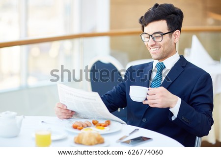Smiling businessman drinking tea or coffee and reading newspaper in cafe