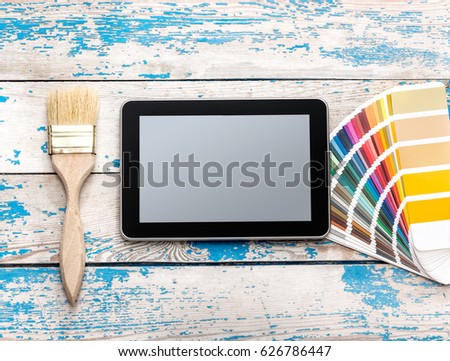 Tablet PC with paintbrush and color swatches book on wooden background.