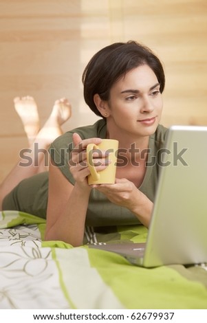 Mid-adult woman having morning coffee in bed, looking at computer.?