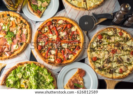 Pizza on paper on a wooden board and pieces of pizza in plates. A lot of pizza on a black table close up. Healthy hot food. Royalty-Free Stock Photo #626812589