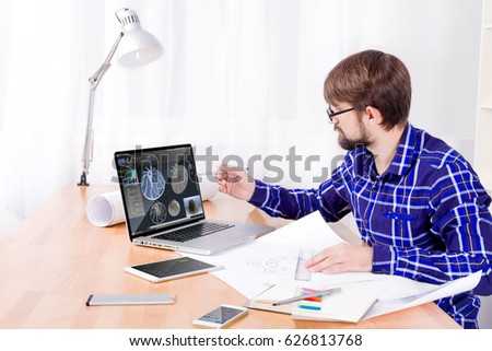 Cad engineer's workplace with laptop with 3d model of turbine on display, drawings, notepad and pen, smartphone and lamp. Young engineer developing new 3d model of turbine for heavy industry  Royalty-Free Stock Photo #626813768
