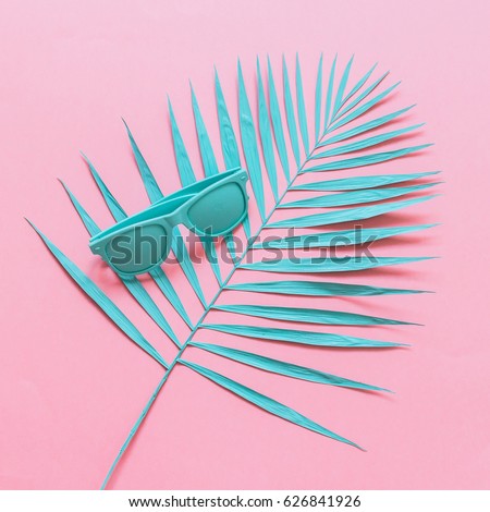 blue sunglasses are on the branch of a palm tree on a pink background. fashion flat lay.