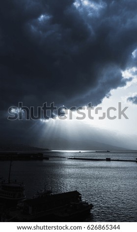 Dark dramatic sky with clouds and sunlight rays over sea. Bay of Izmir. Blue toned photo filter effect