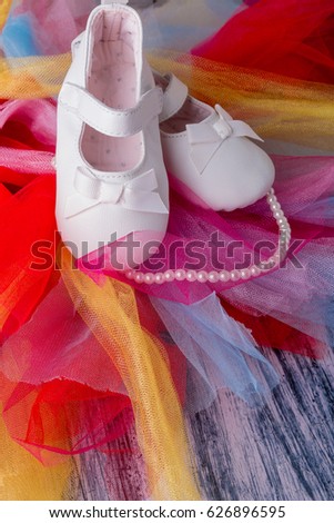 Baby girl white shoes near pearls on colored tulle background