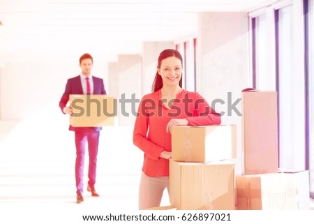 Portrait of confident mid adult businesswoman standing by stacked boxes with male colleague in background at office