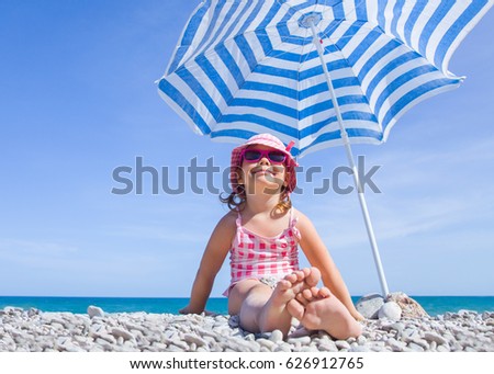 happy little girl at the seaside under an umbrella in the summer