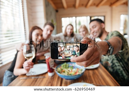 Group of friends having dinner and taking selfie with smartphone at the table