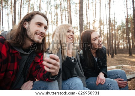 Picture of smiling group of friends sitting outdoors in the forest. Looking aside.