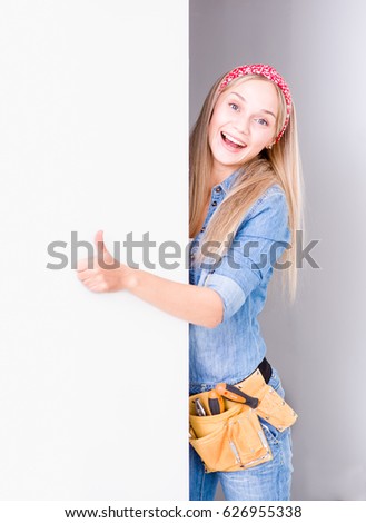 Young woman with tool belt looks above white banner and showing thumbs up