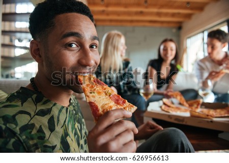 Smiling African man eating pizza surrounded by friends in the house