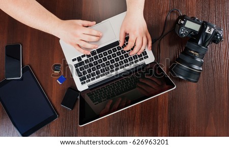 View from above of the hands of a young photographer at work in his office, editing the pictures on his laptop