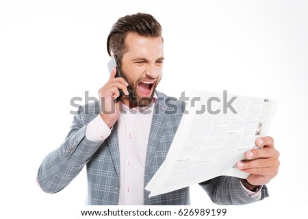 Picture of screaming young man standing isolated over white background while holding gazette and talking by mobile phone. Looking aside.