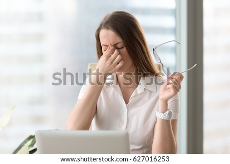 Tired businesswoman holding eyeglasses and massaging nose bridge. Girl feeling discomfort from long wearing glasses at workplace. Exhausted female office worker gather herself for completing work  Royalty-Free Stock Photo #627016253