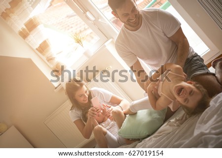 Family playing with their two little girl on bed. Mother making self-picture of fanny scene.