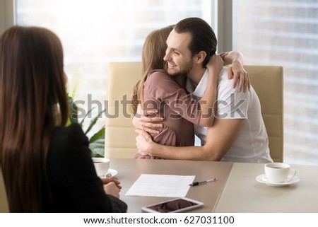 Excited family couple embracing sitting opposite female realtor, happy to buy newly-built apartment or house, purchasing own first property, dream come true, affordable housing for everyone  Royalty-Free Stock Photo #627031100