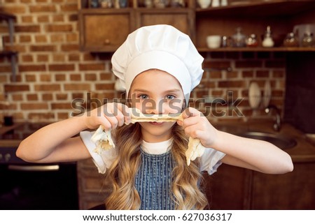 portrait of little girl in chef hat playing with raw dough