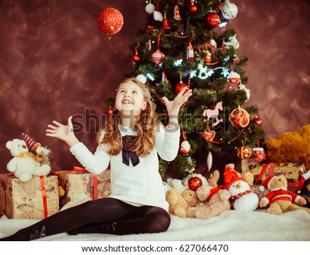 Girl plays with red sparkling toy sitting before Christmas tree