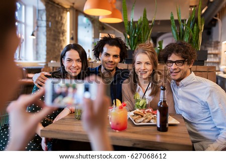 technology, lifestyle and people concept - happy friends with smartphone photographing at bar or cafe