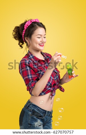 Pinup model blowing soap bubbles over yellow background.