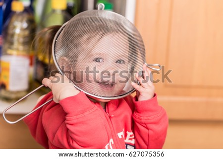 Hiding behind a sieve.Littel funny girl at kitchen playing with vessel