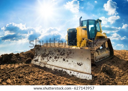 Yellow excavator on new construction site, with the bright sun and nice blue sky in the background Royalty-Free Stock Photo #627143957