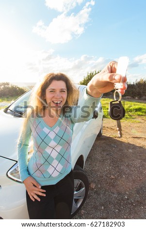 Happy woman driver showing car keys on the background of her automobile