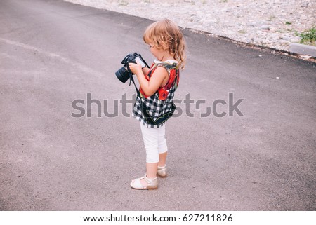 Little girl with big camera in hands outdoors. The concept of development of a capable child, happy family.