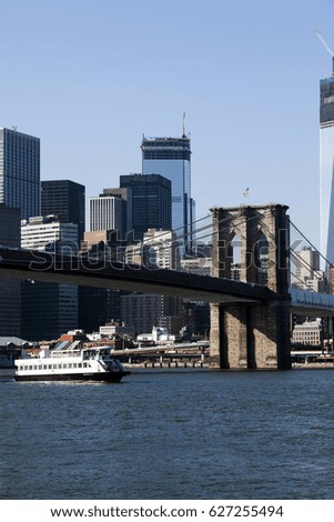 Ferry sailing on the East River with the Brooklyn Bridge stretching above, and the Lower Manhattan skyline in the background.