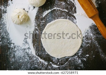 Dough rolling for mini pizza over black wooden background.