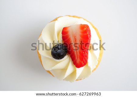 Cupcake with whipped cream, fresh strawberry, blueberry on white background. Top view. Picture for a menu or a confectionery catalog.