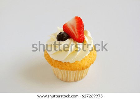 Cupcake with whipped cream, fresh strawberry, blueberry on white background. Picture for a menu or a confectionery catalog.