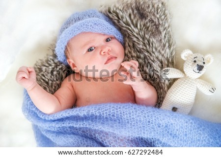 Newborn baby in knitted cap and with a toy bear lying on a fur blanket.
