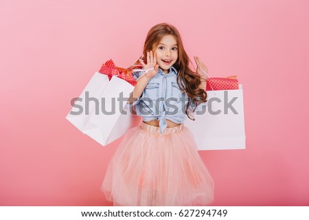 Pretty joyful young girl in tulle skirt, with long brunette hair walking with white packages on pink background. Lovely sweet moments of little princess, pretty friendly child having fun to camera Royalty-Free Stock Photo #627294749