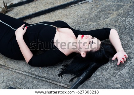 Beautiful young woman (girl) brunette in tight black dress lies on the surface. Portrait to the waist. Shooting outdoors, soft selective focus